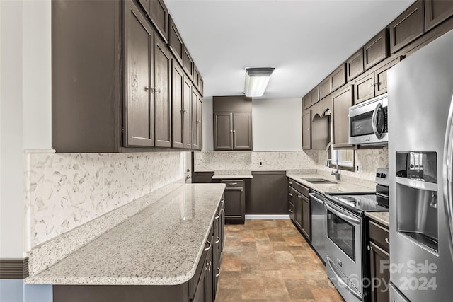 kitchen with dark brown cabinets, stainless steel appliances, light stone counters, and sink