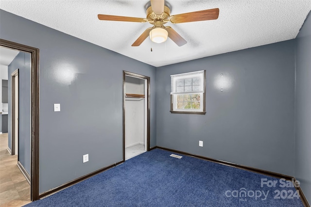 unfurnished bedroom with a textured ceiling, light colored carpet, a closet, and ceiling fan