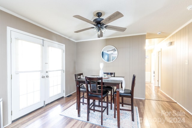 dining room with ceiling fan, french doors, light hardwood / wood-style flooring, wooden walls, and ornamental molding