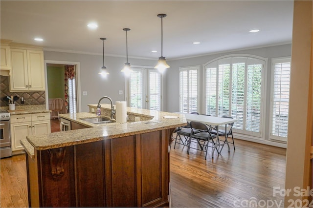 kitchen with a kitchen island with sink, tasteful backsplash, decorative light fixtures, light stone counters, and wood-type flooring