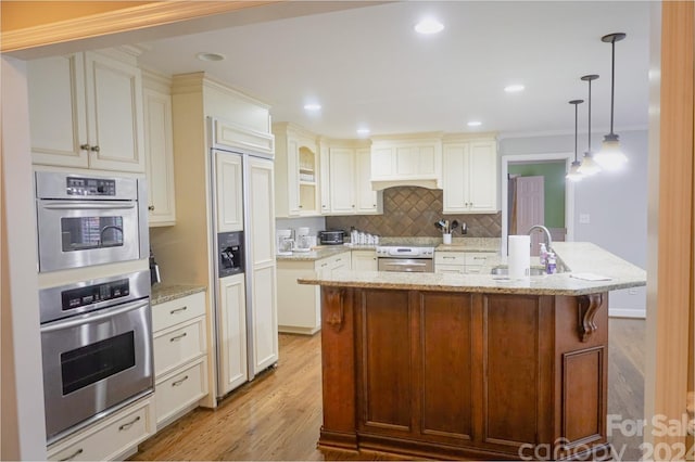 kitchen featuring sink, hanging light fixtures, light stone counters, light hardwood / wood-style floors, and a kitchen island with sink