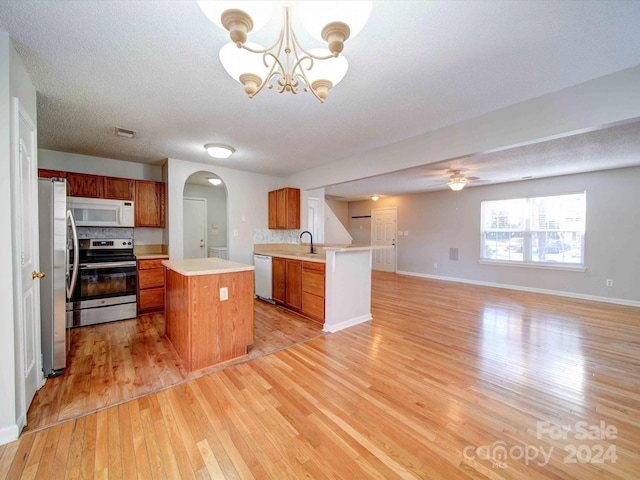 kitchen featuring backsplash, stainless steel appliances, decorative light fixtures, light hardwood / wood-style floors, and a kitchen island