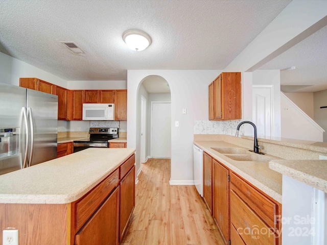 kitchen featuring appliances with stainless steel finishes, a textured ceiling, light hardwood / wood-style flooring, and sink