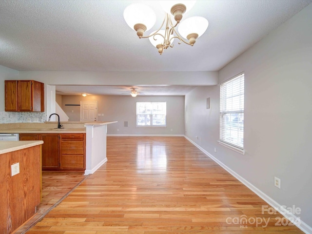 kitchen featuring dishwasher, sink, kitchen peninsula, pendant lighting, and light wood-type flooring