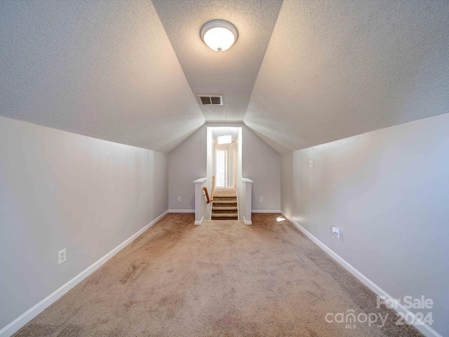 bonus room with a textured ceiling, light colored carpet, and lofted ceiling