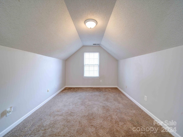 additional living space with a textured ceiling, carpet floors, and vaulted ceiling