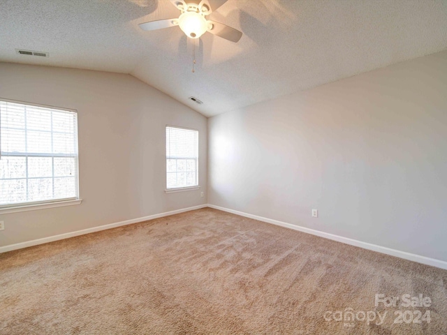 carpeted spare room with a textured ceiling, vaulted ceiling, and ceiling fan