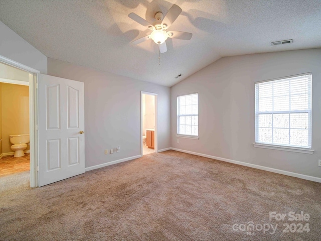 unfurnished bedroom featuring light carpet, vaulted ceiling, ensuite bath, and ceiling fan