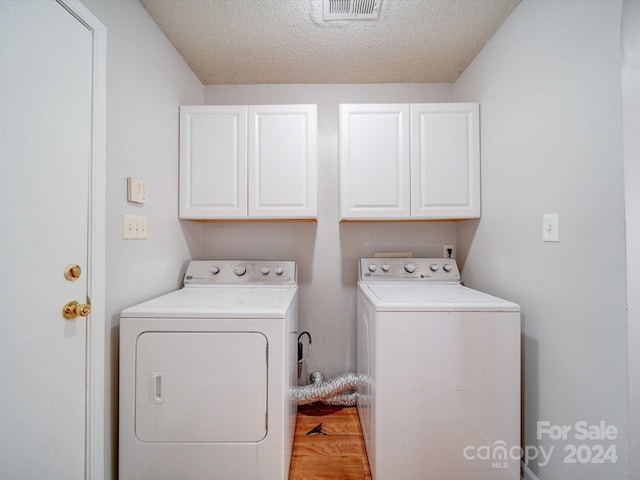 laundry area featuring hardwood / wood-style flooring, cabinets, a textured ceiling, and independent washer and dryer