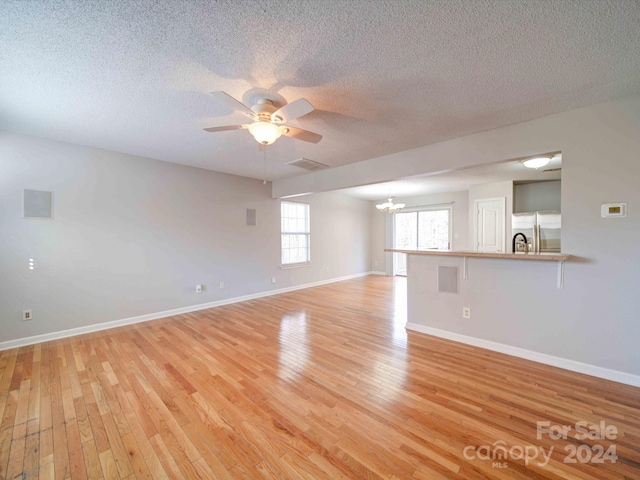 empty room with ceiling fan with notable chandelier, light hardwood / wood-style floors, and a textured ceiling