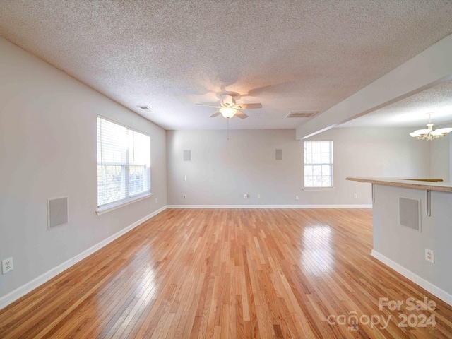 unfurnished room with ceiling fan with notable chandelier, light wood-type flooring, and a textured ceiling