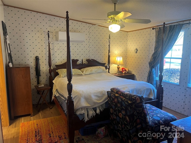 bedroom featuring an AC wall unit, ceiling fan, light wood-type flooring, a textured ceiling, and ornamental molding