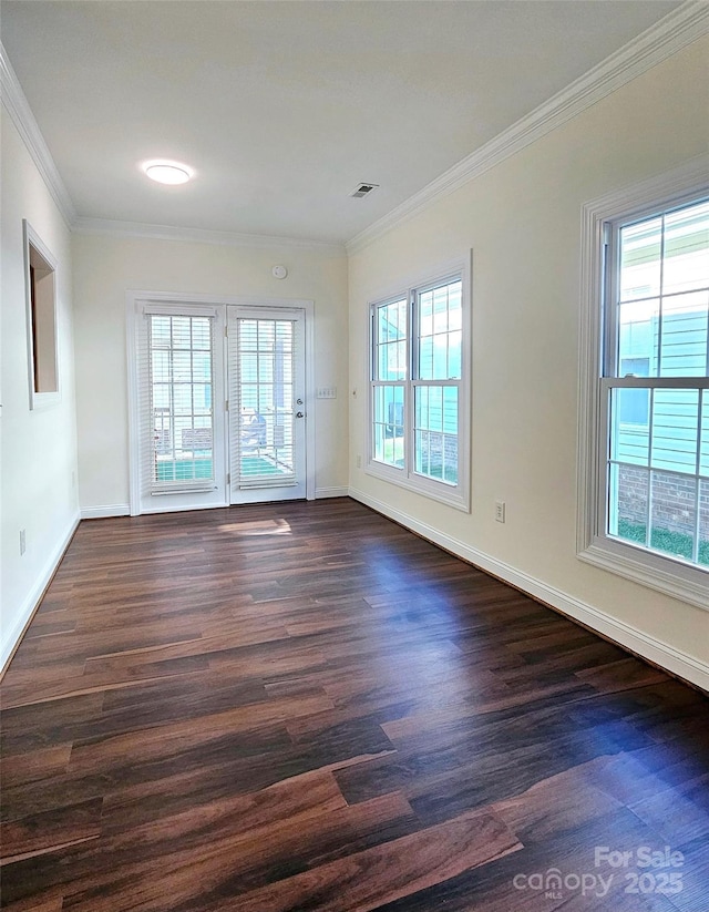 spare room featuring dark wood-type flooring, a wealth of natural light, and crown molding