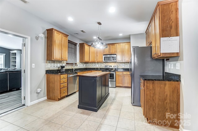 kitchen featuring appliances with stainless steel finishes, backsplash, dark stone counters, hanging light fixtures, and a center island