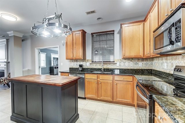 kitchen with a center island, sink, appliances with stainless steel finishes, light tile patterned floors, and dark stone counters