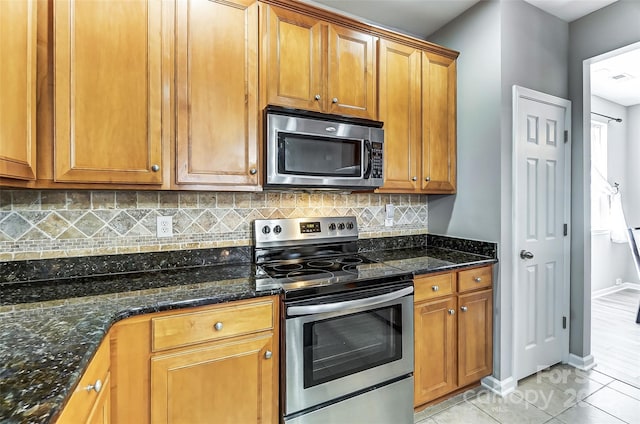 kitchen featuring light tile patterned floors, stainless steel appliances, dark stone countertops, and backsplash