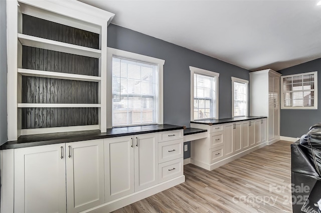 kitchen featuring light wood-type flooring, built in desk, and white cabinets