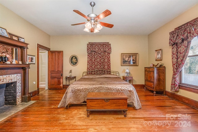 bedroom featuring hardwood / wood-style floors, ceiling fan, and a brick fireplace