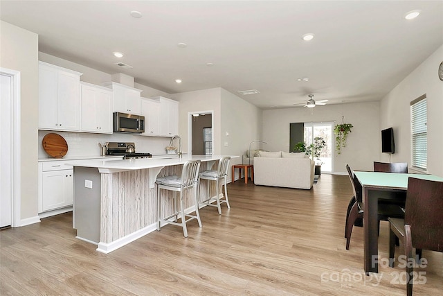 kitchen featuring white cabinetry, light hardwood / wood-style flooring, stainless steel appliances, and a center island with sink