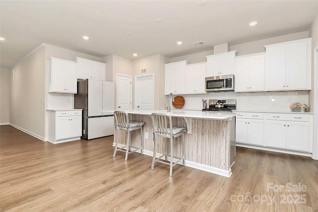 kitchen featuring white cabinetry, appliances with stainless steel finishes, light hardwood / wood-style floors, and an island with sink