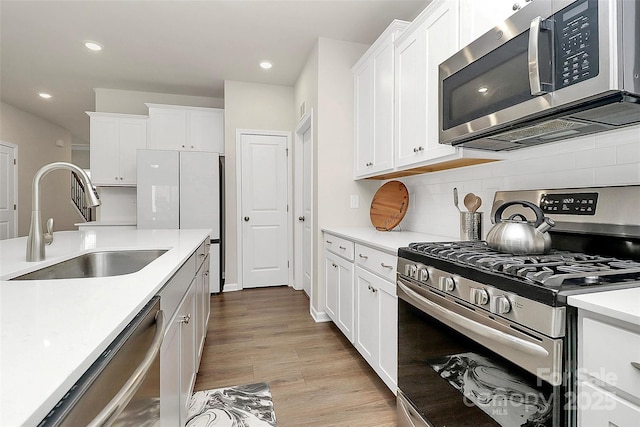 kitchen with sink, light hardwood / wood-style flooring, appliances with stainless steel finishes, white cabinetry, and backsplash