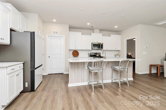 kitchen with white cabinetry, appliances with stainless steel finishes, light hardwood / wood-style floors, and an island with sink