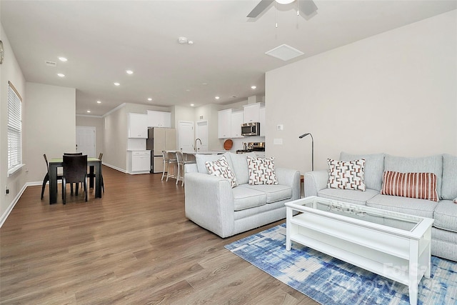 living room featuring ceiling fan, sink, and light wood-type flooring