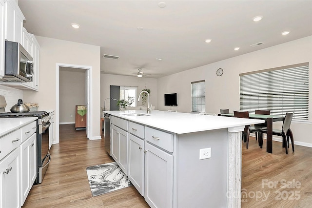 kitchen featuring sink, white cabinets, a kitchen island with sink, stainless steel appliances, and light hardwood / wood-style flooring