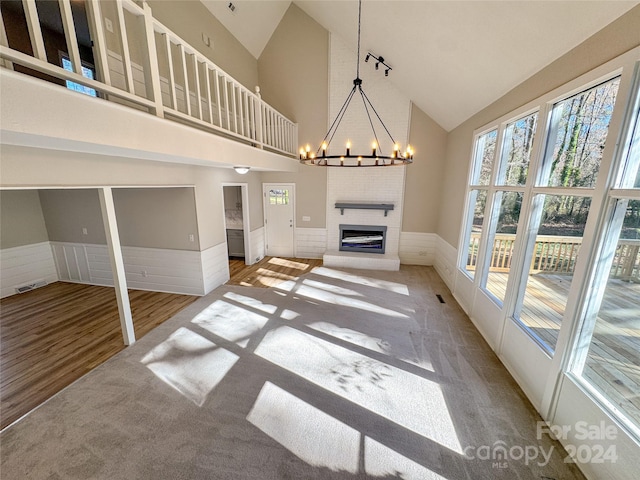 unfurnished living room featuring hardwood / wood-style flooring, a large fireplace, high vaulted ceiling, and an inviting chandelier