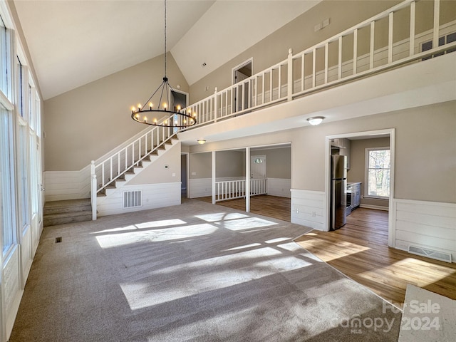 unfurnished living room with hardwood / wood-style floors, high vaulted ceiling, and a notable chandelier