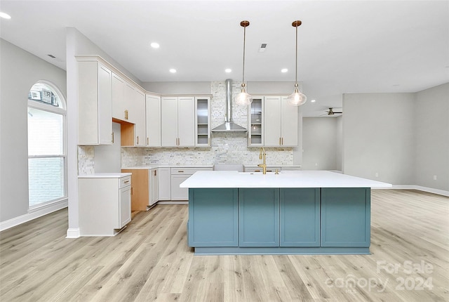 kitchen with decorative light fixtures, light hardwood / wood-style flooring, white cabinetry, and wall chimney exhaust hood