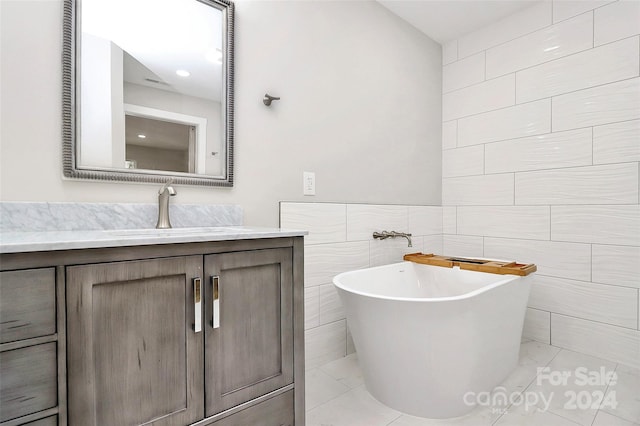 bathroom with vanity, a tub to relax in, and tile walls