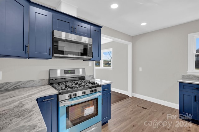 kitchen featuring light stone countertops, blue cabinets, stainless steel appliances, and wood-type flooring