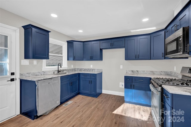 kitchen with sink, stainless steel appliances, light stone counters, blue cabinets, and light hardwood / wood-style floors