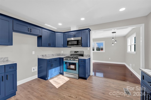 kitchen featuring hanging light fixtures, light wood-type flooring, blue cabinetry, appliances with stainless steel finishes, and light stone counters