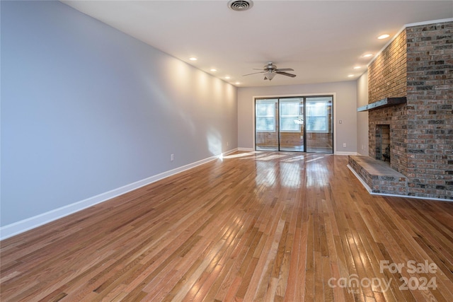 unfurnished living room featuring hardwood / wood-style floors, a brick fireplace, ceiling fan, and brick wall