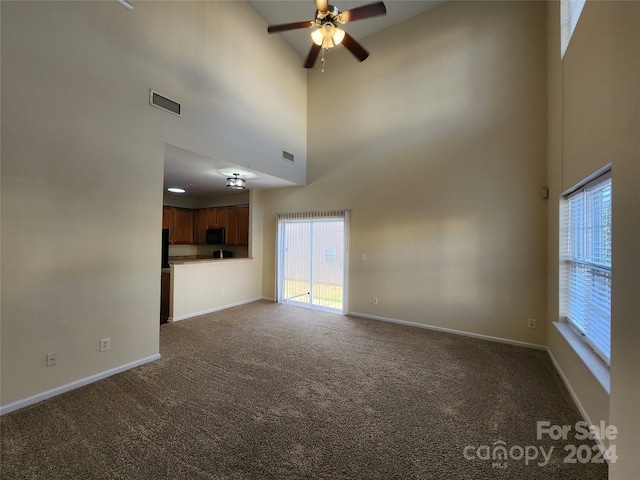 unfurnished living room with a high ceiling, dark carpet, and ceiling fan