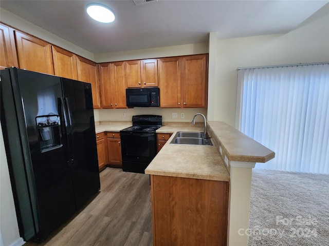 kitchen featuring a breakfast bar, black appliances, kitchen peninsula, sink, and wood-type flooring