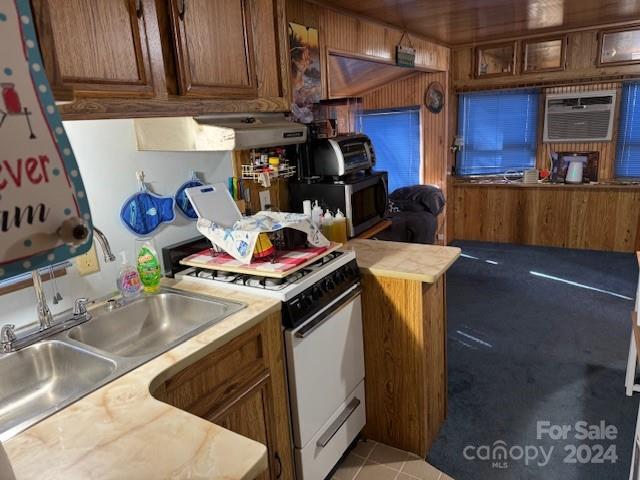 kitchen featuring white gas range, wood walls, sink, and light tile patterned floors