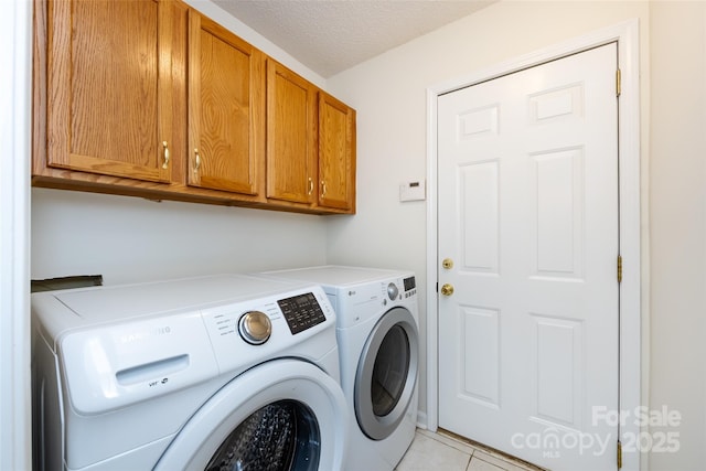 laundry area with cabinet space, a textured ceiling, separate washer and dryer, and light tile patterned flooring