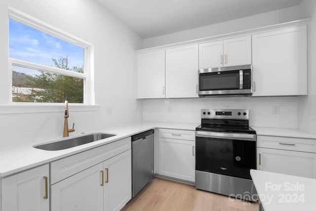 kitchen with white cabinetry, sink, stainless steel appliances, backsplash, and light wood-type flooring