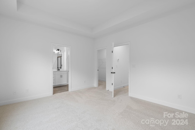 unfurnished bedroom with connected bathroom, a walk in closet, and light colored carpet