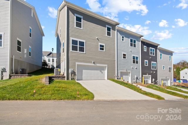 rear view of property with a lawn, central AC, and a garage