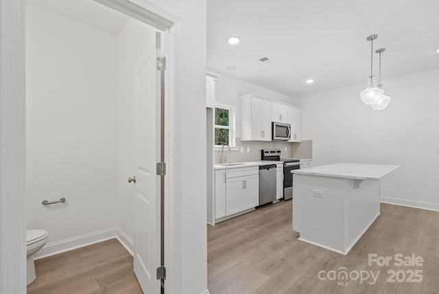 kitchen with sink, appliances with stainless steel finishes, white cabinetry, light hardwood / wood-style floors, and decorative light fixtures