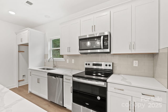 kitchen with sink, appliances with stainless steel finishes, white cabinetry, tasteful backsplash, and light stone countertops