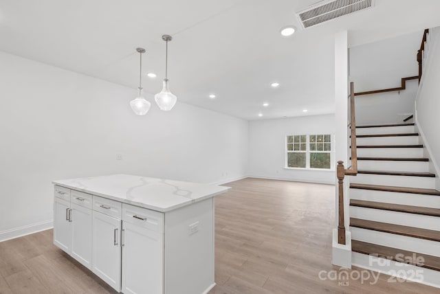 kitchen with white cabinetry, decorative light fixtures, a center island, and light hardwood / wood-style floors