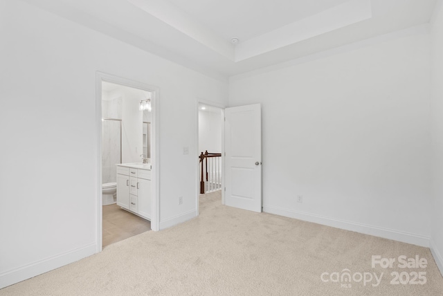 unfurnished bedroom with connected bathroom, a tray ceiling, and light colored carpet