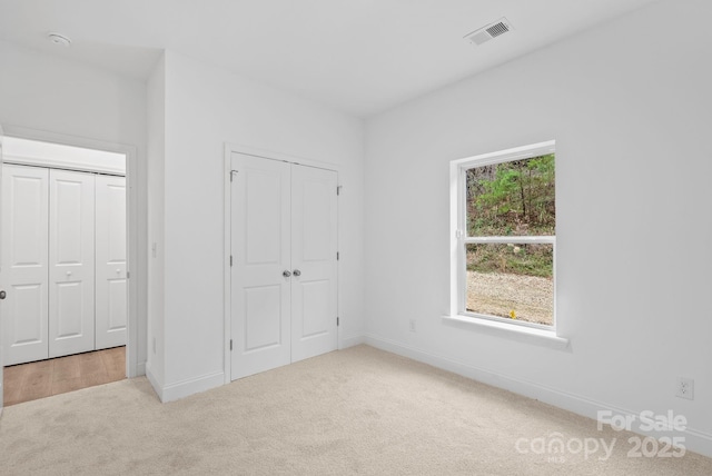 unfurnished bedroom with light colored carpet and two closets