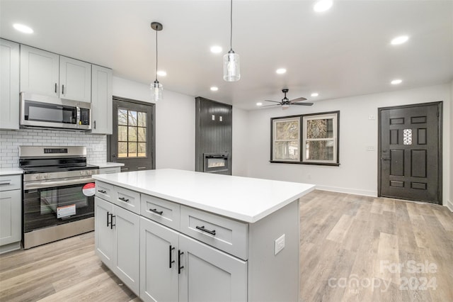 kitchen with ceiling fan, a center island, stainless steel appliances, light hardwood / wood-style flooring, and pendant lighting