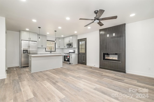 kitchen featuring pendant lighting, light hardwood / wood-style flooring, a fireplace, appliances with stainless steel finishes, and a kitchen island